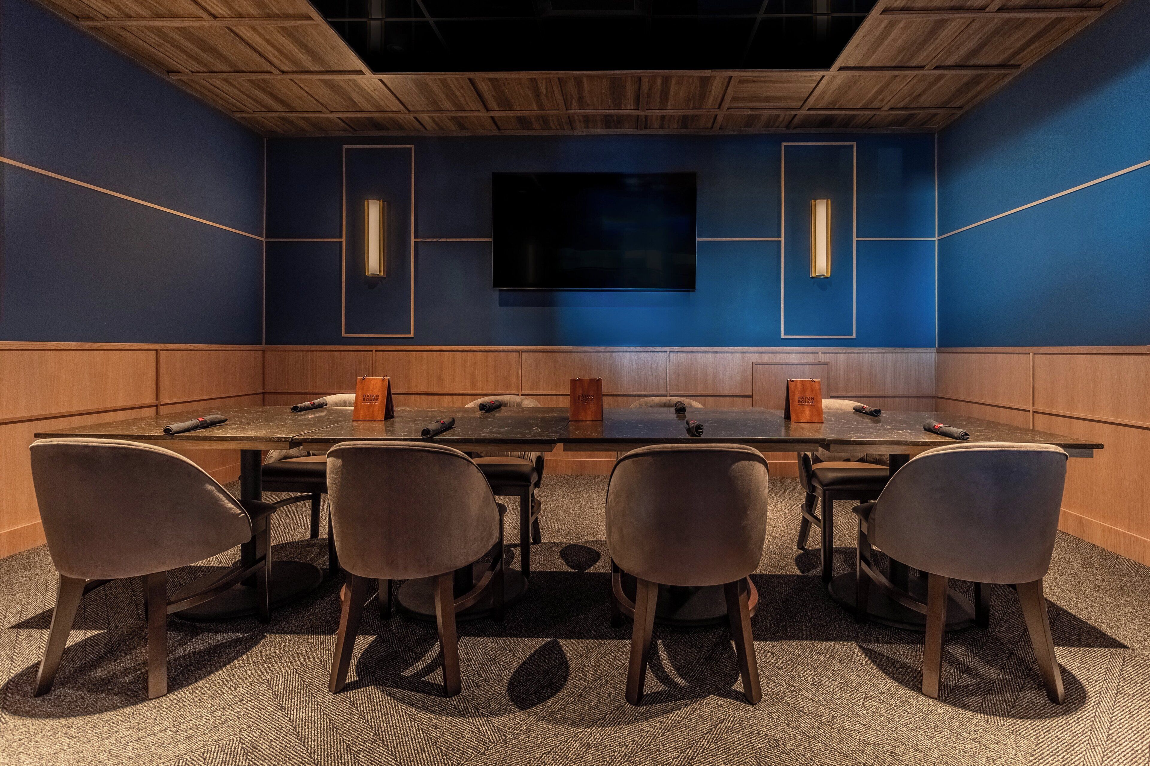 A conference room with a large table, four chairs, a TV screen, and wooden paneling on the walls.