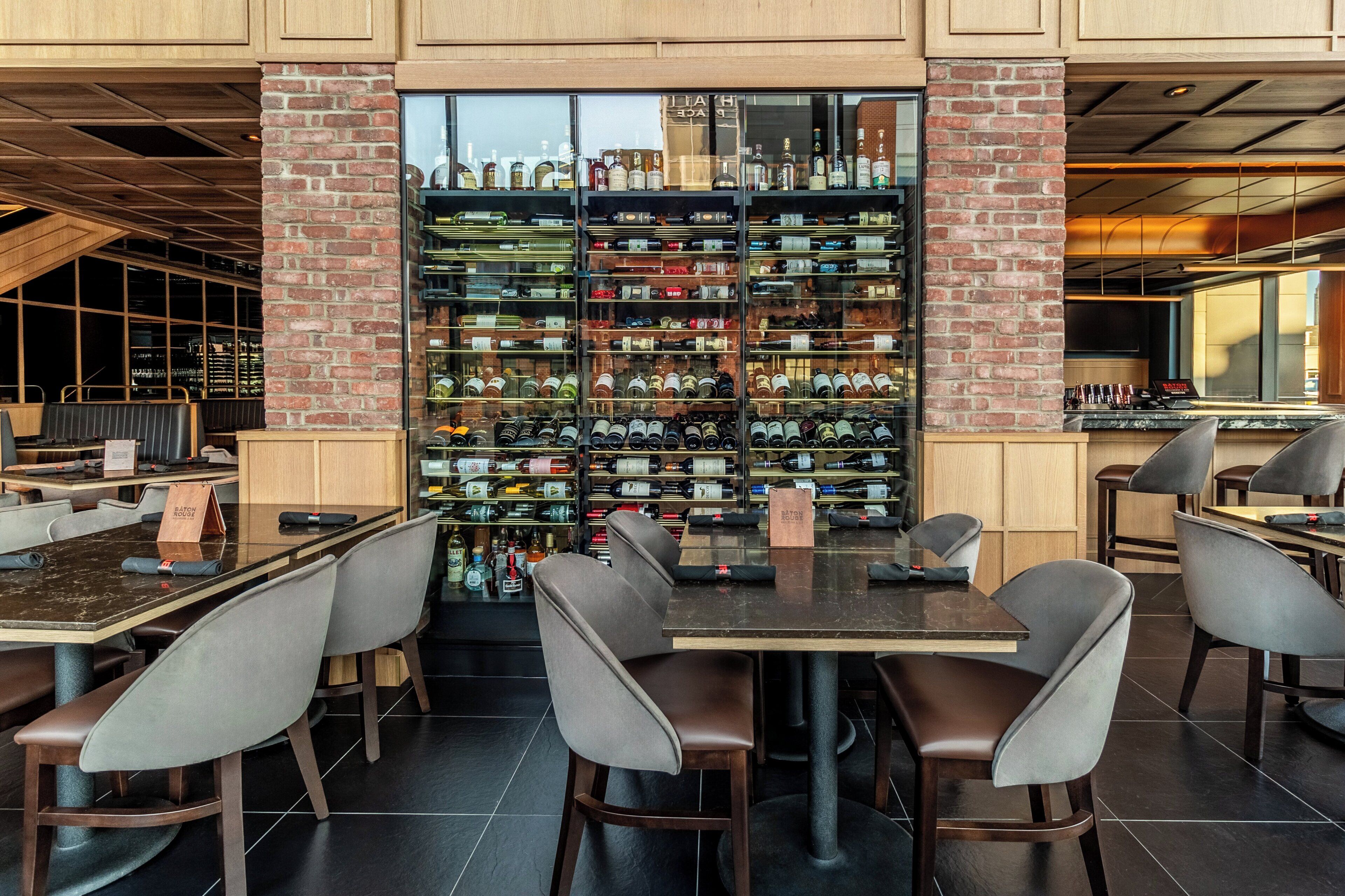 Un restaurante con una pared de ladrillo que exhibe botellas de vino, asientos modernos y techo de madera.