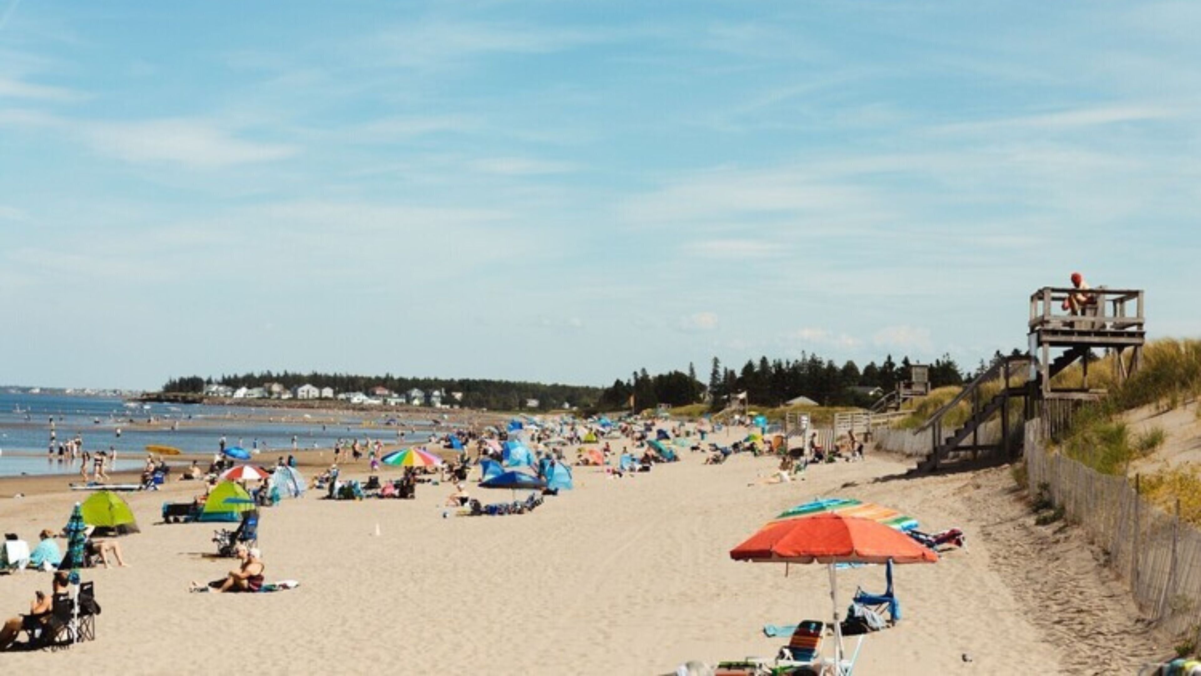 Una playa con gente, tiendas de campaña y una torre de salvavidas.