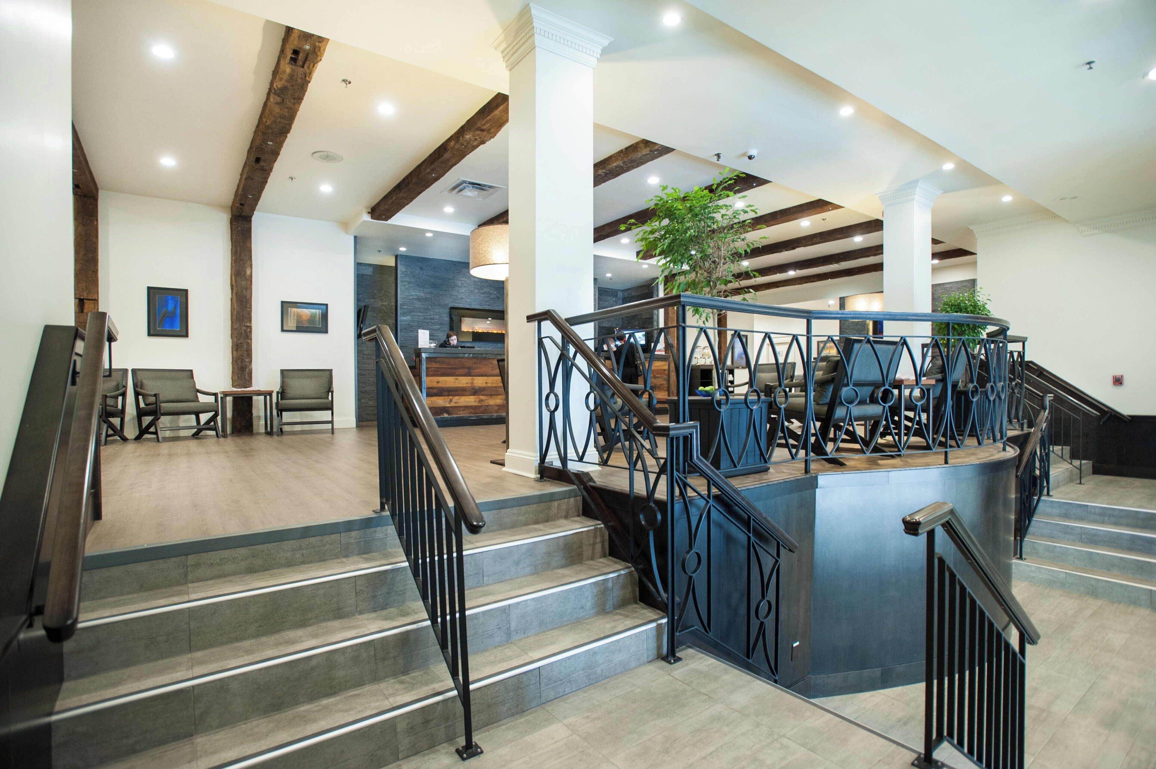 Un moderno vestíbulo de hotel con una escalera, zona de estar y mostrador de recepción.