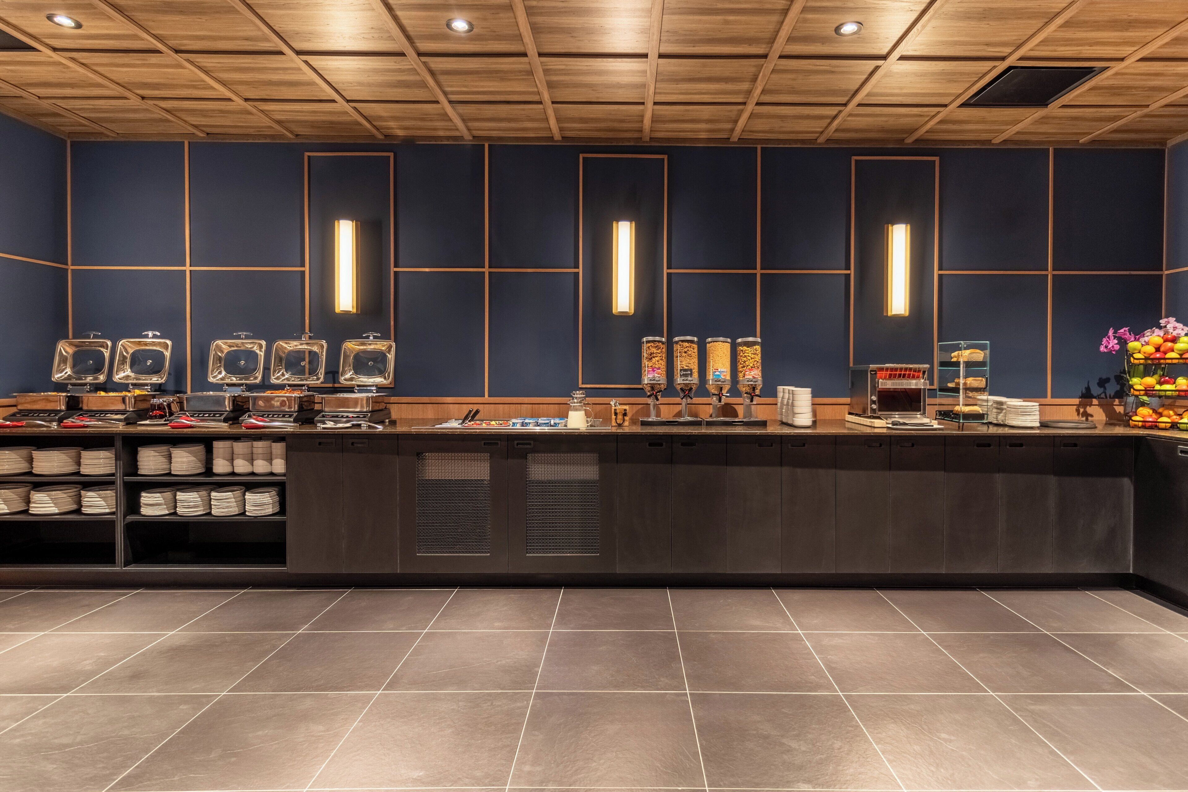 Un área de cocina moderna con pared azul oscuro, techo de madera y una encimera larga con diversos electrodomésticos y espacio de almacenamiento.