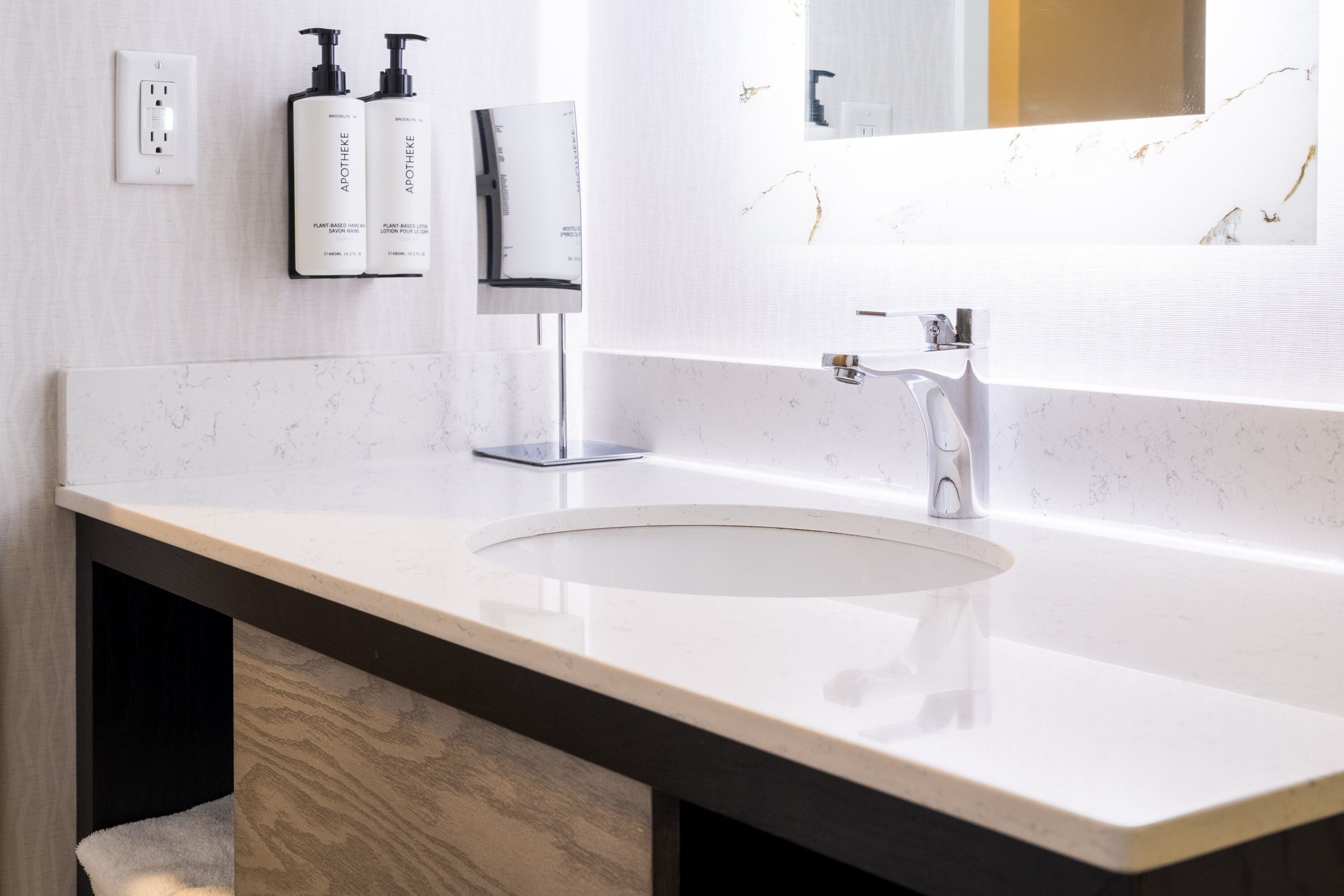 A modern bathroom with a white sink, a mirror, and two bottles of lotion on the wall.