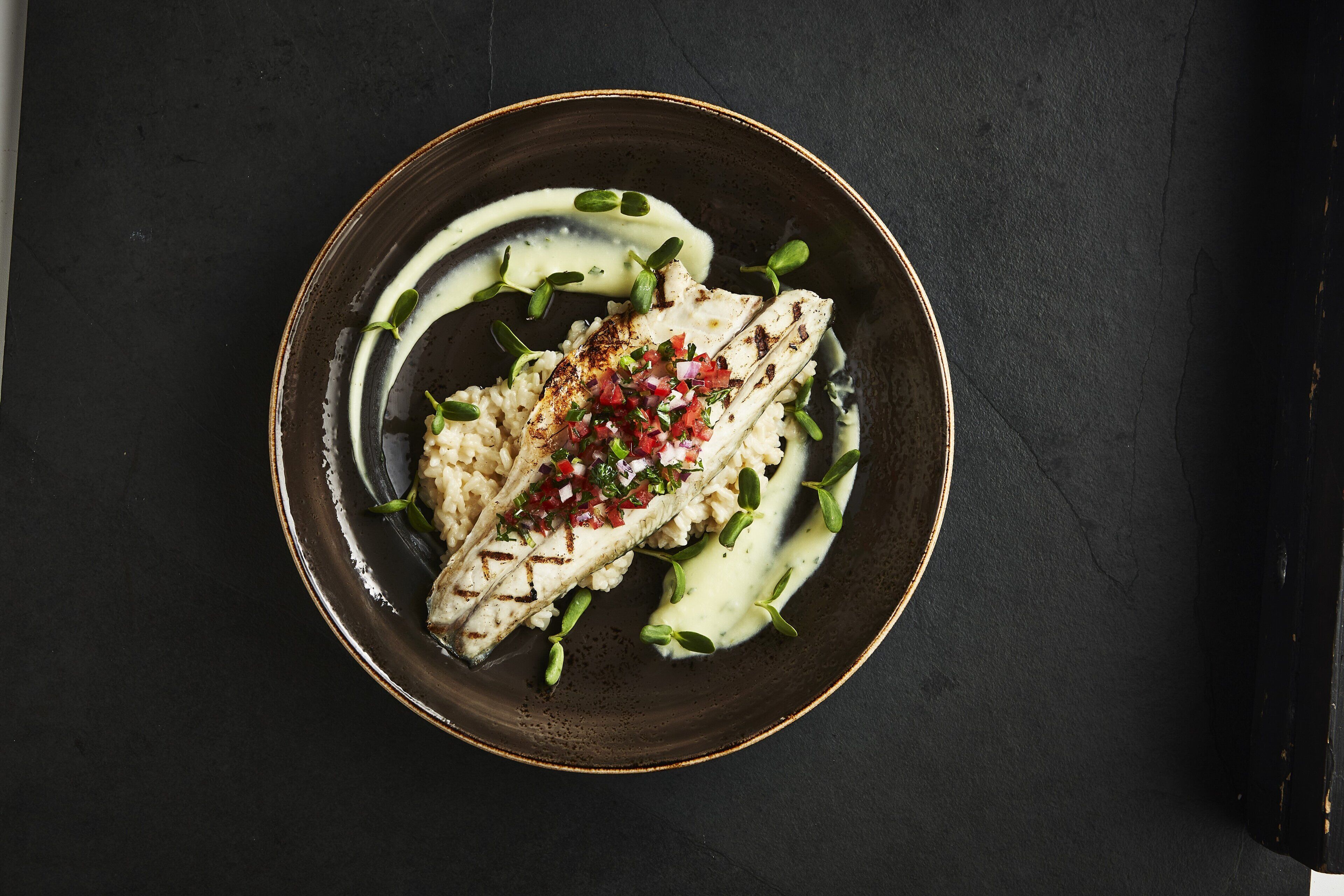 A plate with grilled fish, a creamy sauce, and a garnish of red onions and herbs.