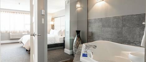 A modern hotel bathroom with a large bathtub, a shower, and a glass-enclosed walk-in closet.