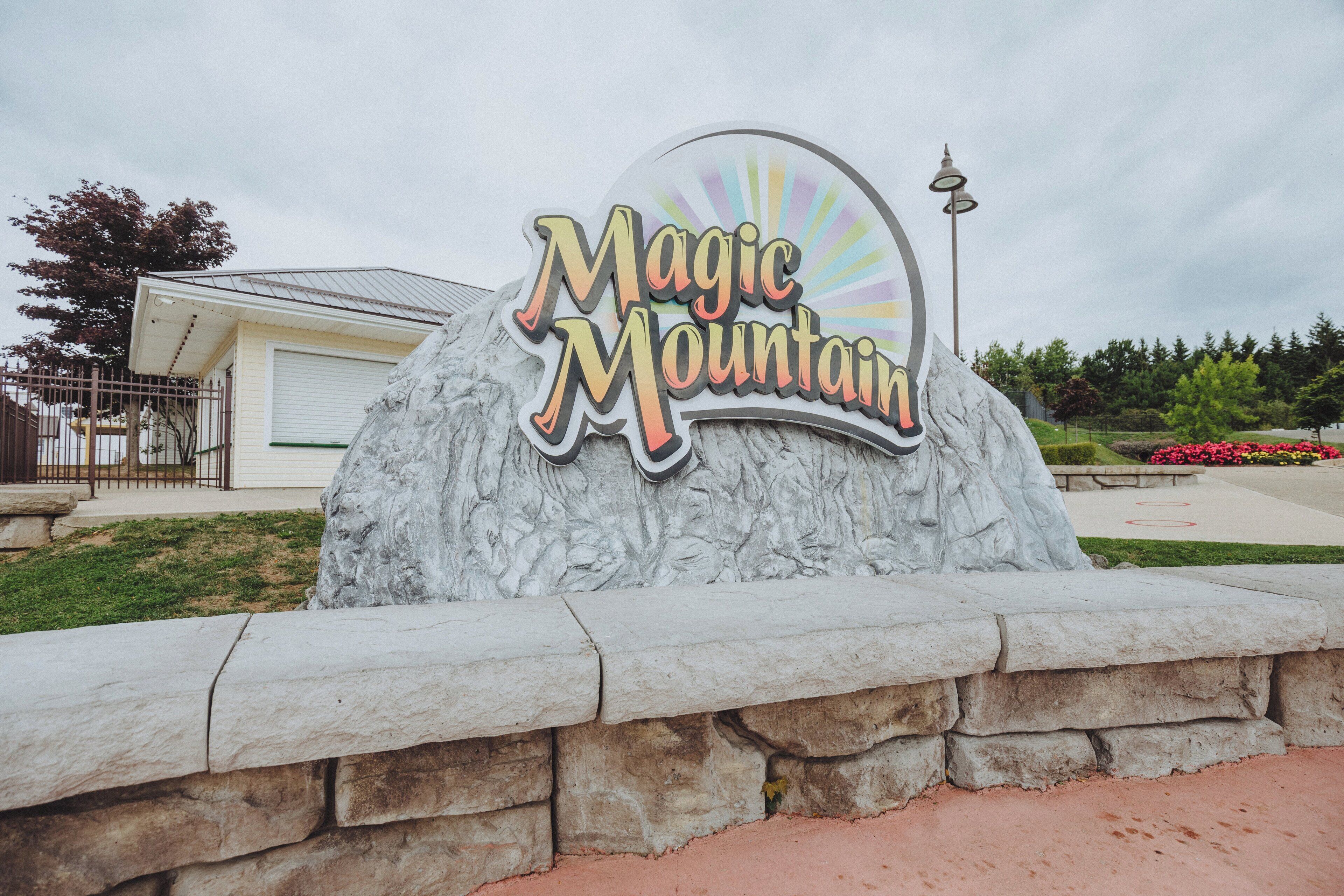 A large rock with the words 'Magic Mountain' on it, surrounded by a stone wall.
