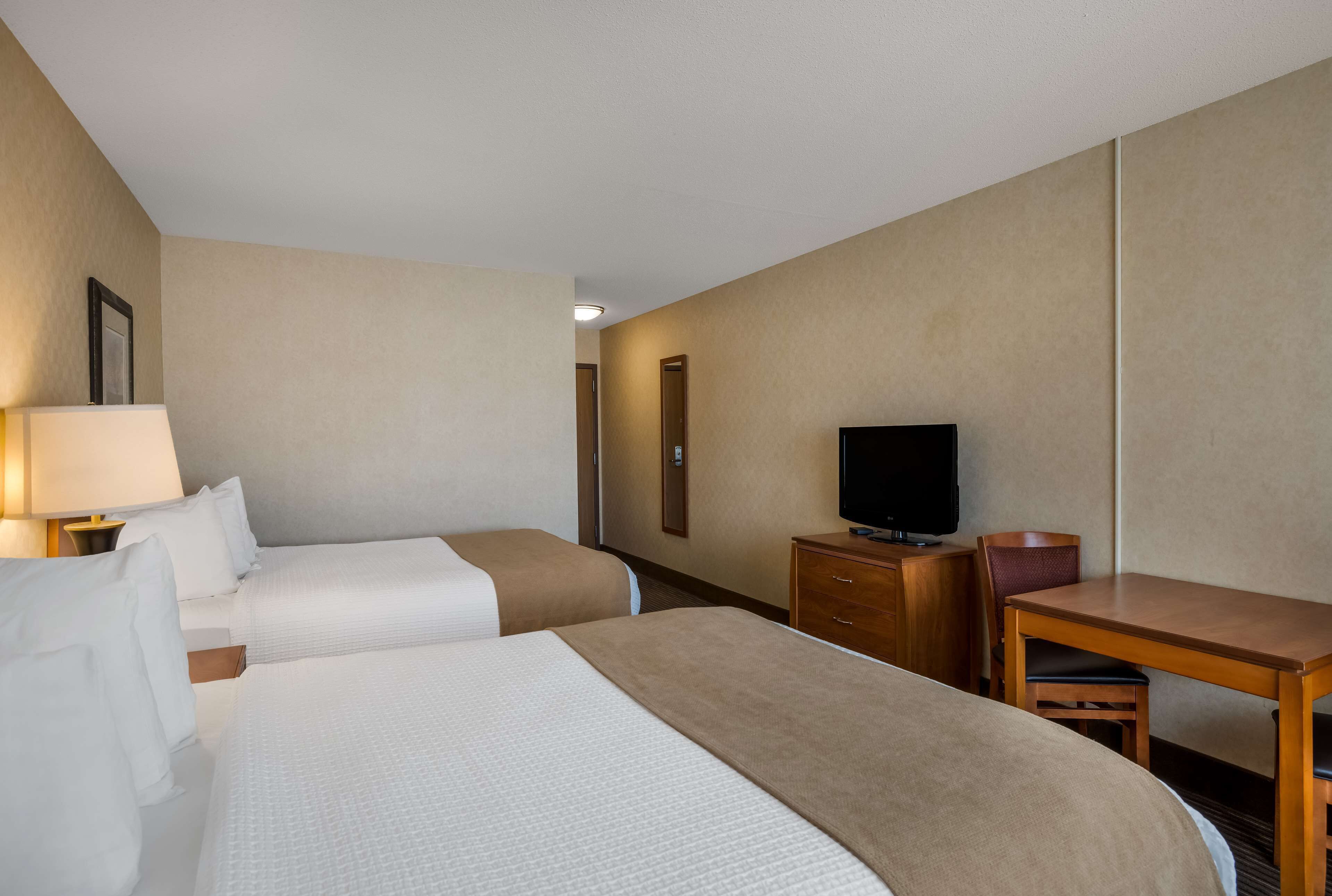A hotel room with two beds, a desk, a television, and a mirror.