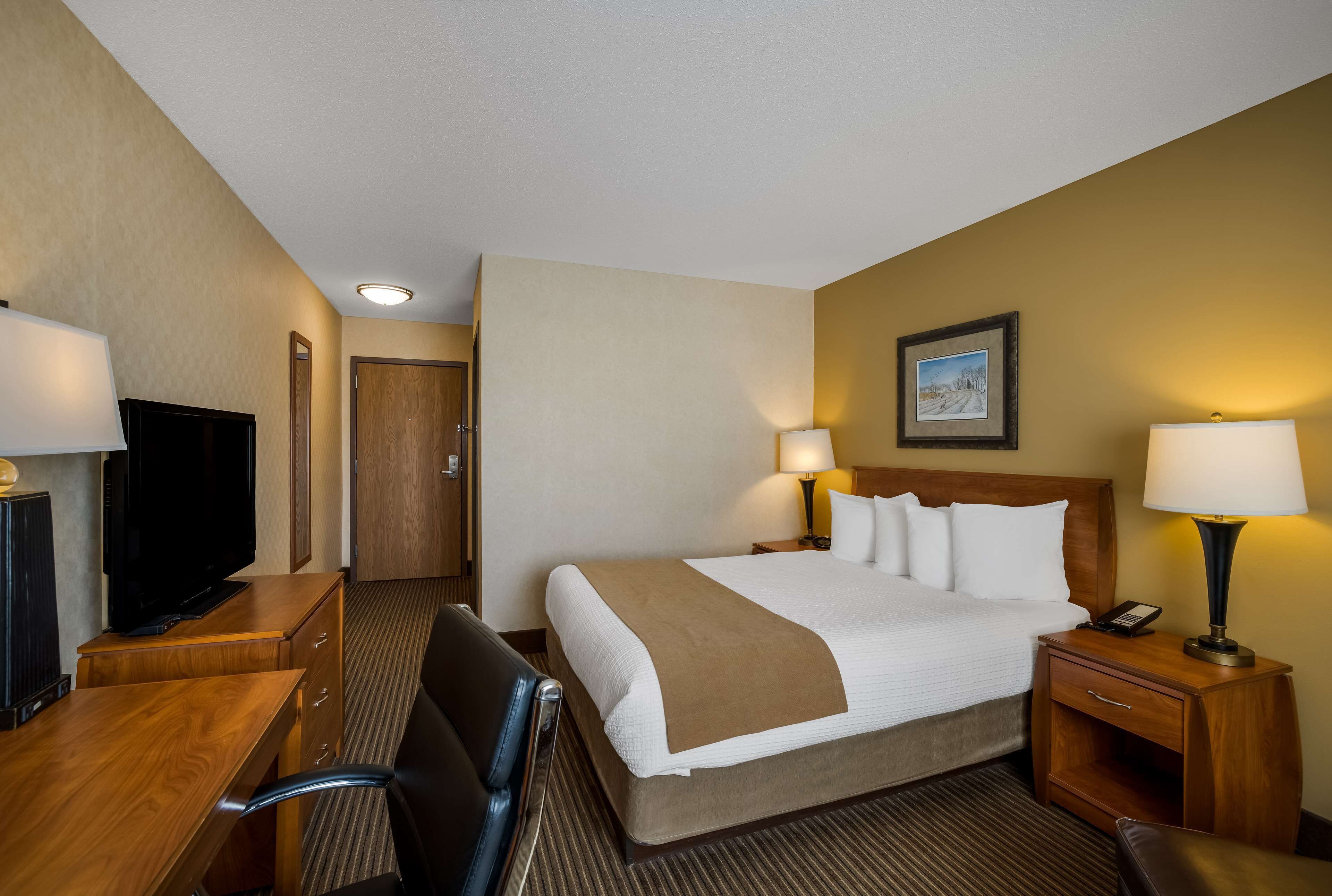Una habitación de hotel con cama, lámparas de noche, televisor, escritorio y silla.