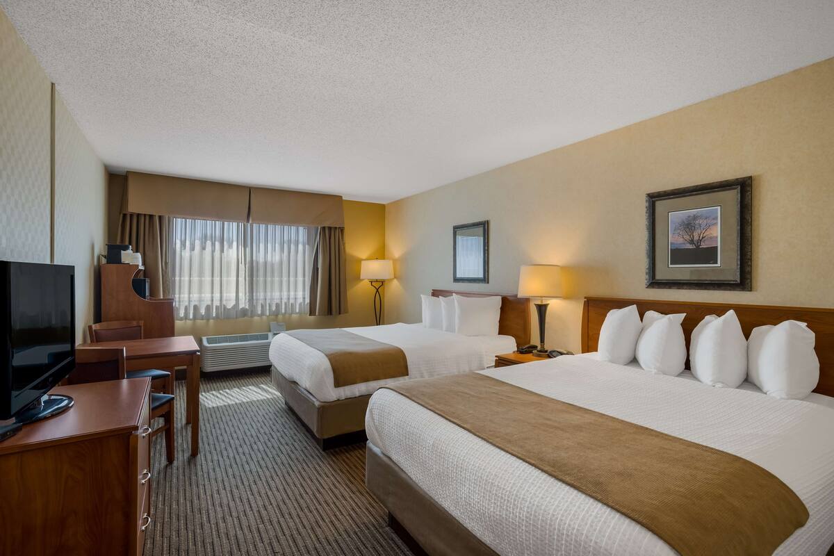 A hotel room with two beds, a desk with a TV, and a large window with curtains.