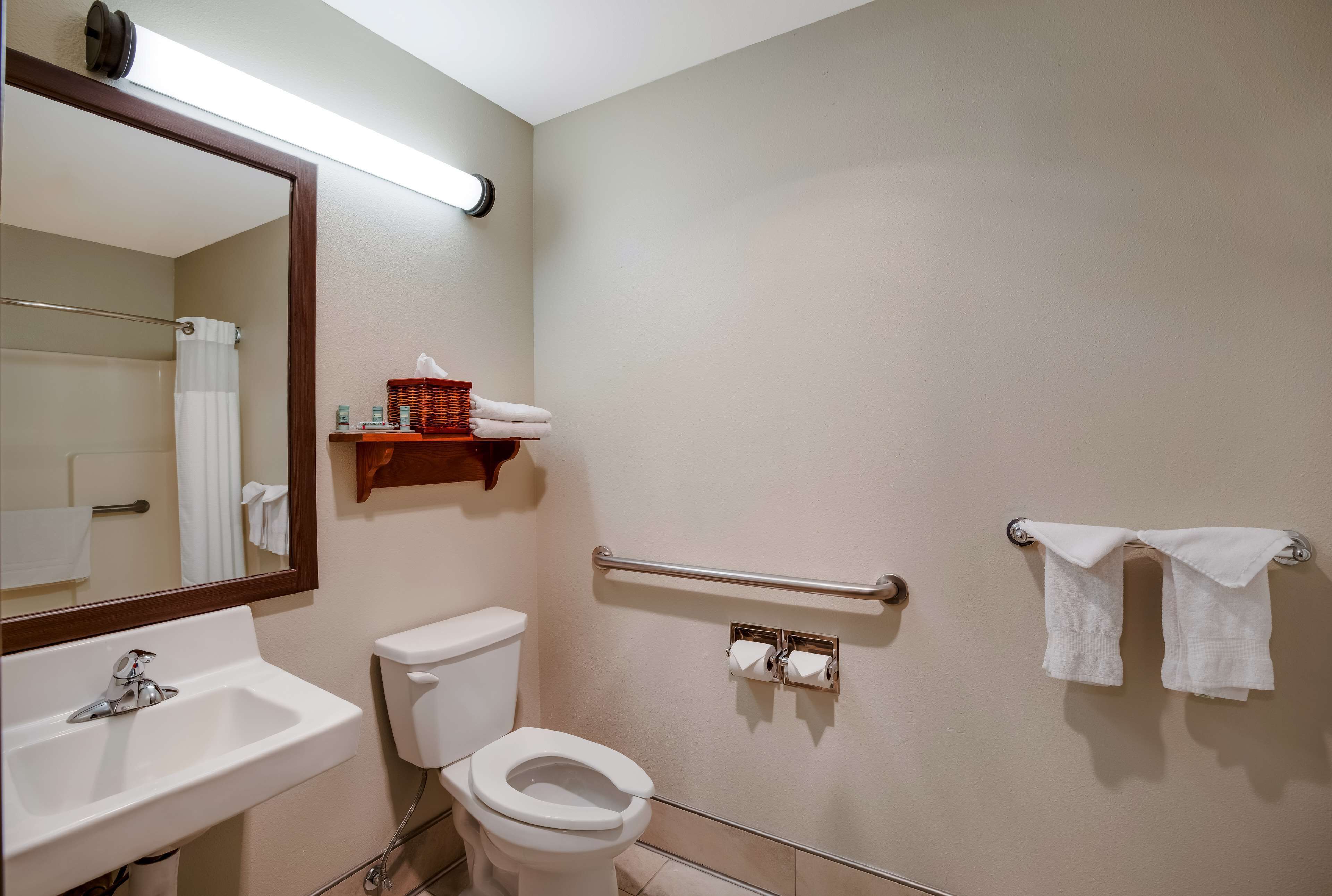 Un baño con lavamanos, inodoro, espejo, toallero y barras de apoyo.
