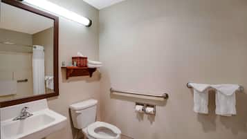 Un baño con lavamanos, inodoro, espejo, toallero y barras de apoyo.