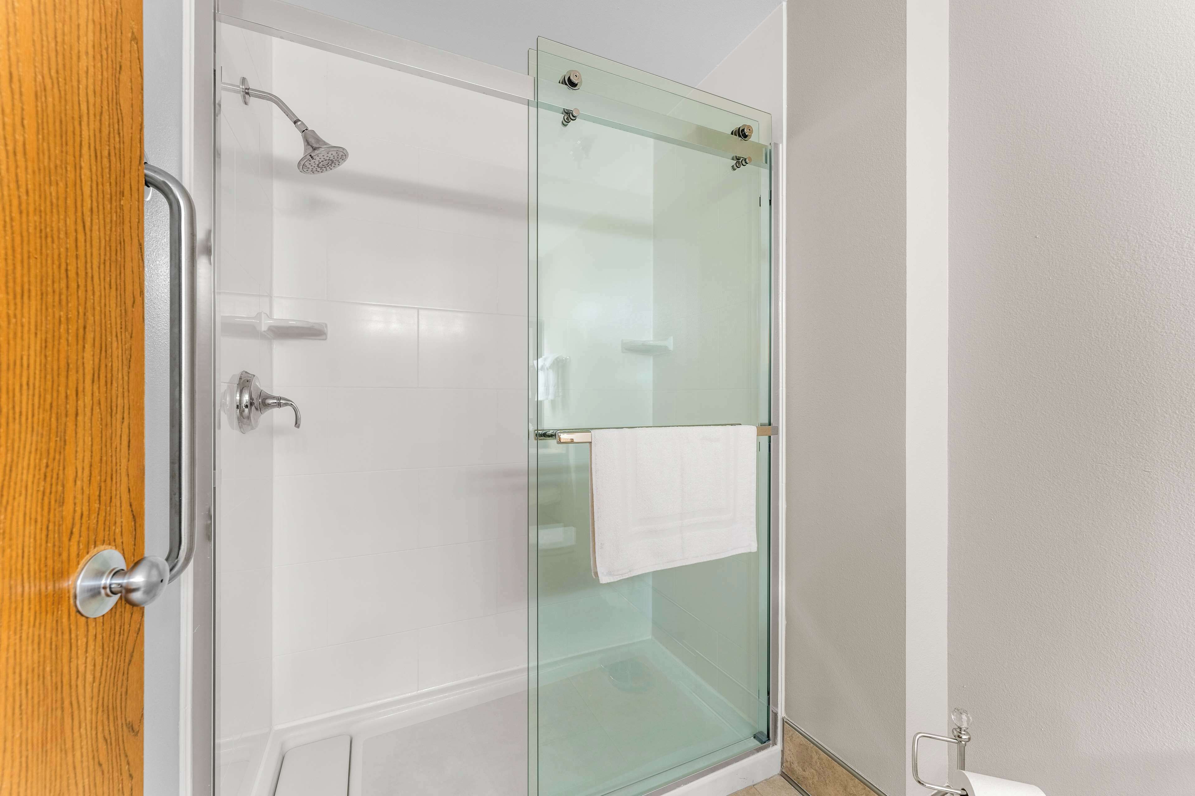 A glass-enclosed shower with a white towel hanging on the door, a wooden door frame, and a white tiled wall.