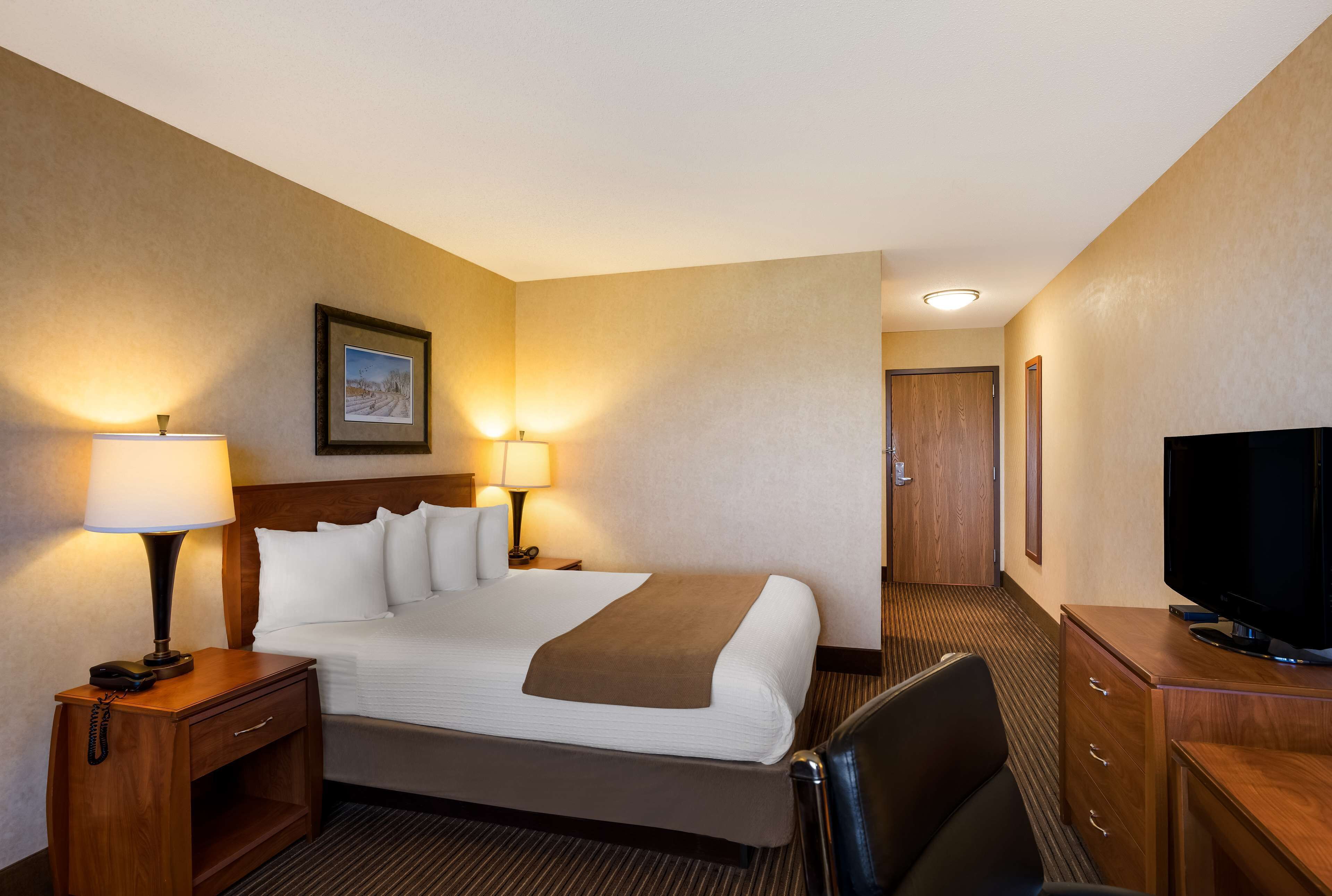 A hotel room with a bed, bedside lamps, a television, and a wooden nightstand.