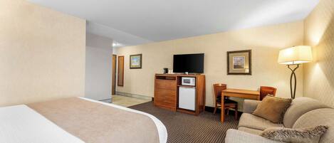 Ein Hotelzimmer mit Bett, Sofa, Schreibtisch, Fernseher, Mikrowelle und Lampe.