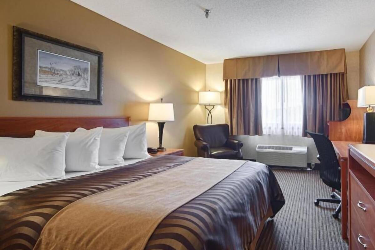 A hotel room with a bed, a desk, a chair, a lamp, a heater, and a window with curtains.