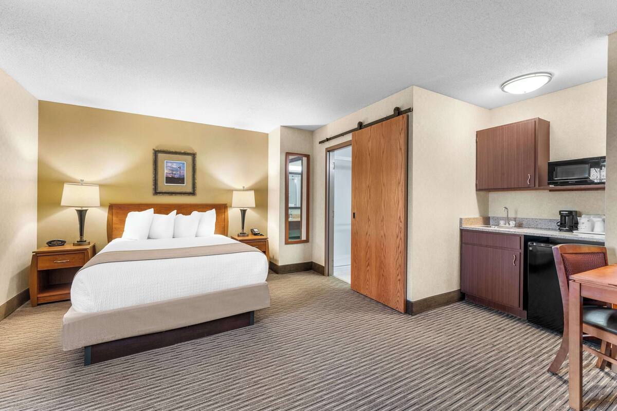 A hotel room with a bed, bedside lamps, a small desk, a microwave, and a kitchenette.