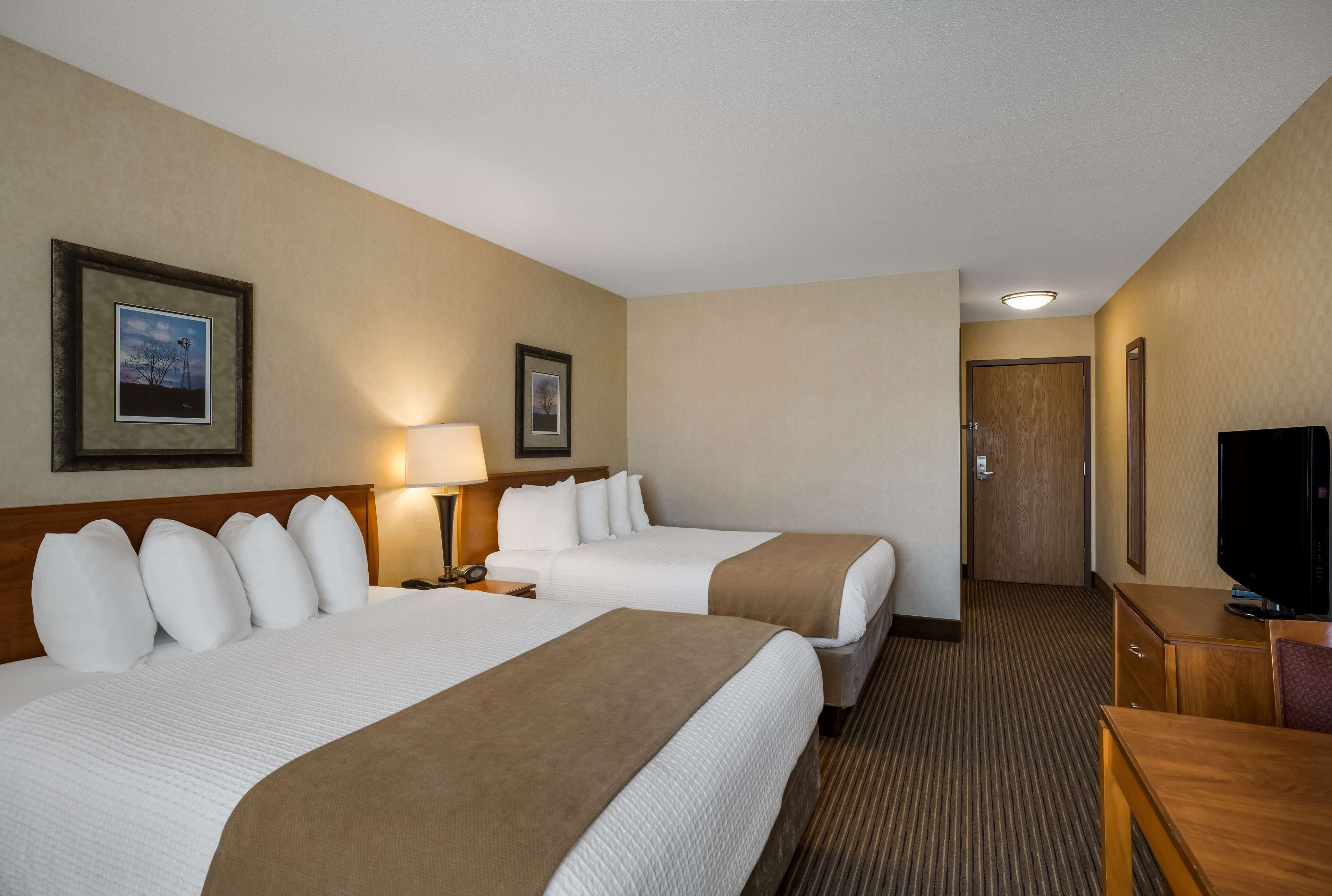 A hotel room with two beds, a TV, a desk, and a door leading to a hallway.