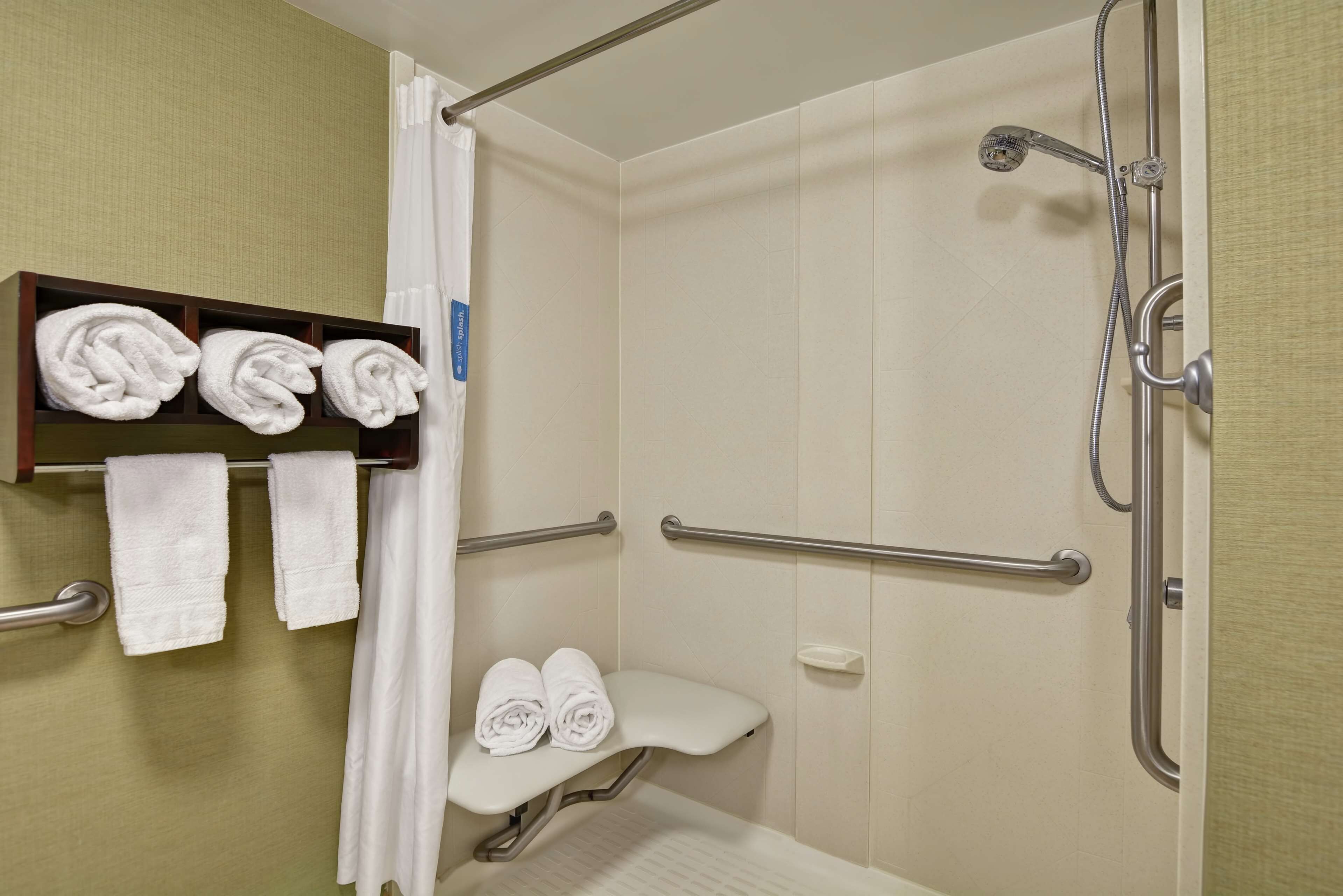 Un baño con ducha, inodoro y estante con toallas.