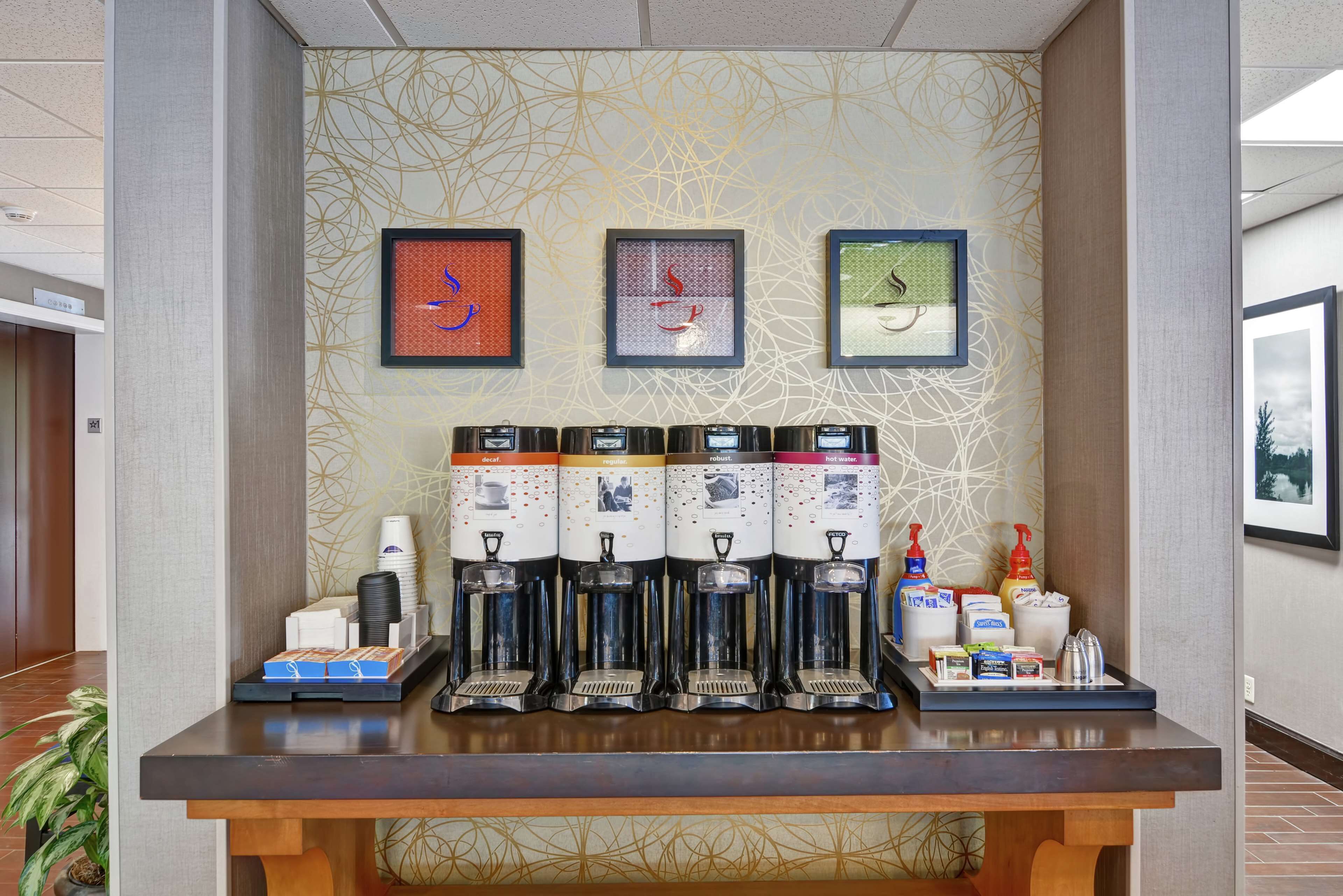 A coffee station with multiple dispensers, a tray with coffee cups, and a framed artwork on the wall.