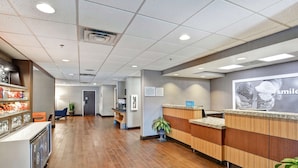 A hotel reception area with a wooden reception desk, a blue sign, and a large poster on the wall. - Hampton Inn Charlotte-Gastonia (Gastonia)