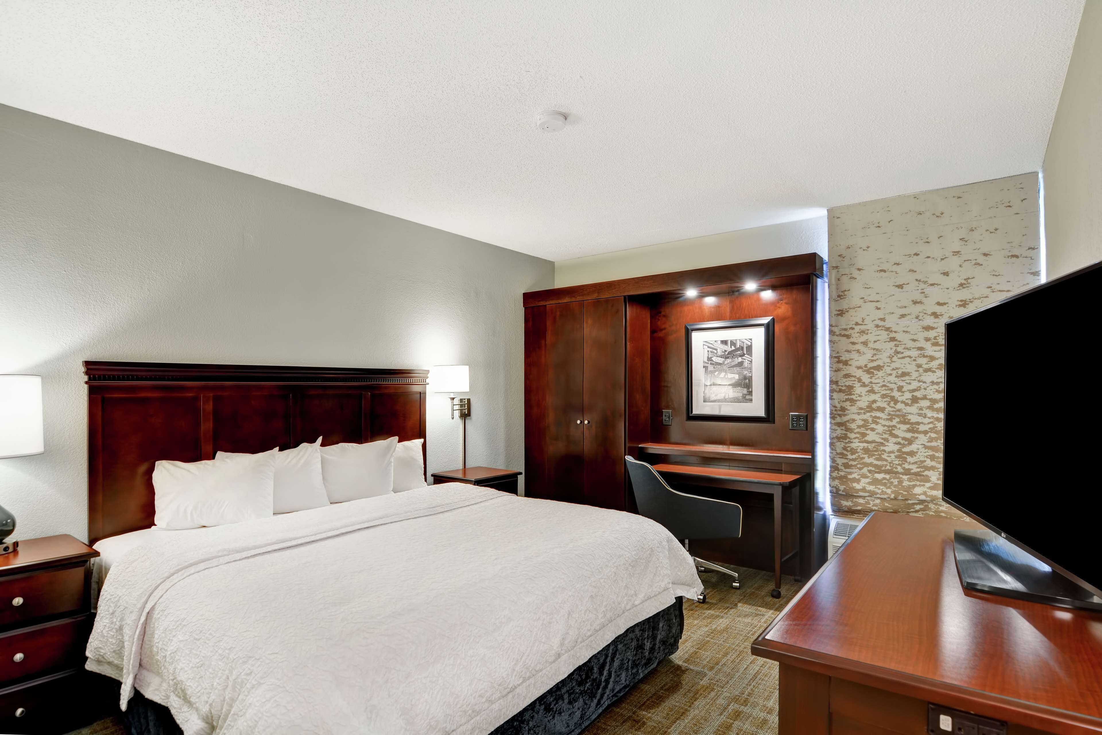 Ein Hotelzimmer mit einem großen Bett, einem Schreibtisch, einem Sessel und einem Fernseher.