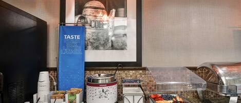 A breakfast buffet setup with coffee machines, a coffee station, and various food options like cereal, mixed nuts, and berries.
