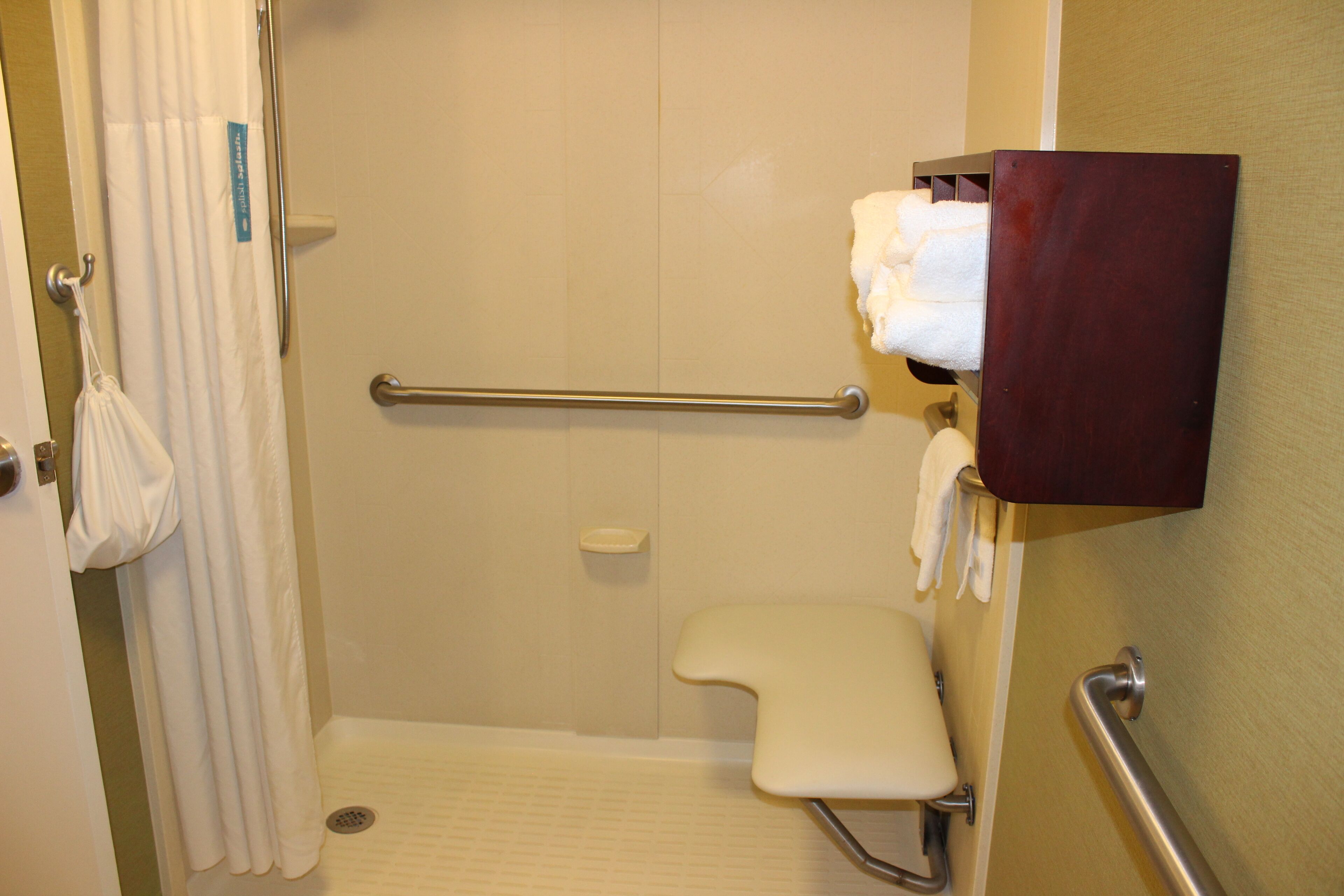 Un baño con ducha, barra de apoyo y un inodoro con asiento elevado.