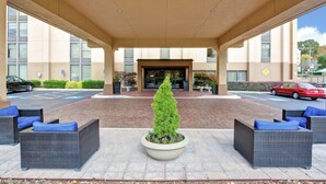 A covered outdoor seating area with wicker furniture and a central planter with a coniferous tree. - Hampton Inn Charlotte-Gastonia (Gastonia)