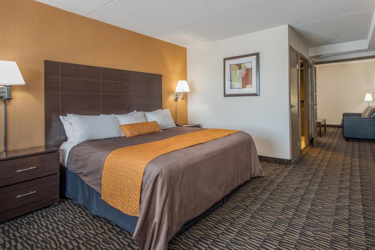Een hotelkamer met een bed, nachtkastjes, een bureau, een stoel en een deur naar een andere kamer.