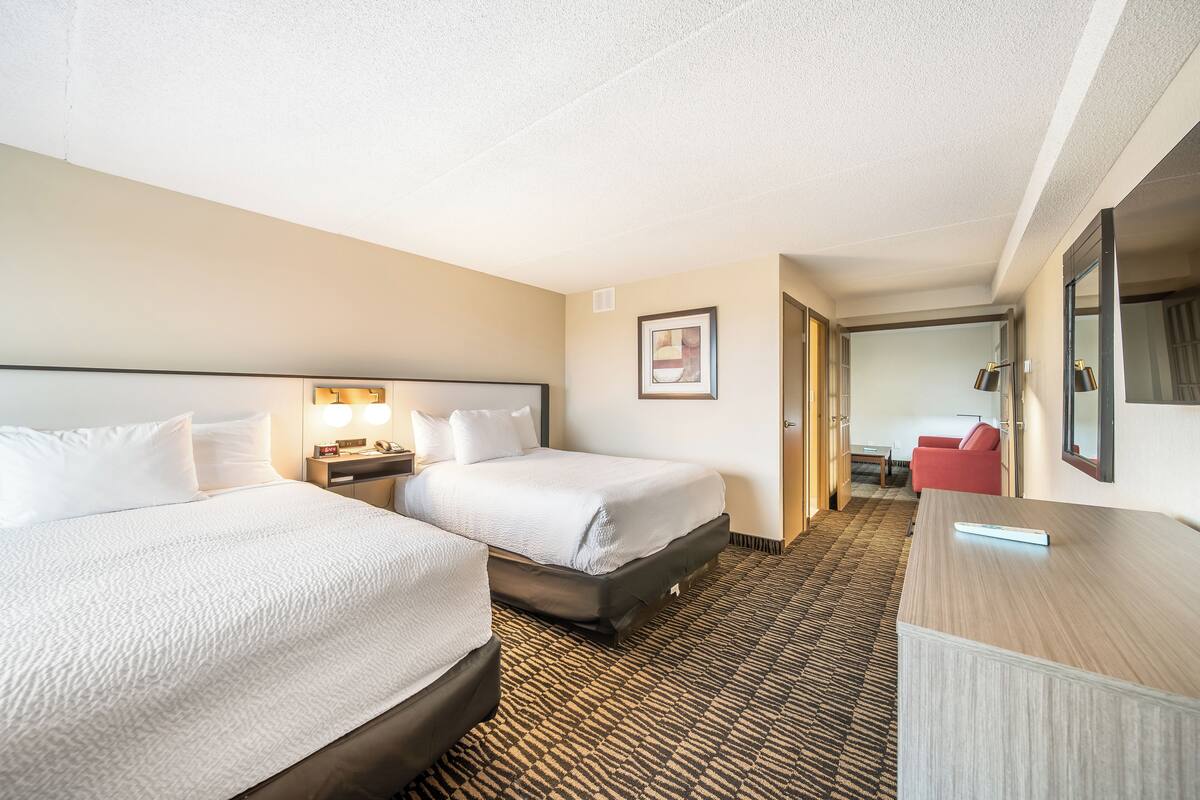Ein Hotelzimmer mit zwei Betten, einem Schreibtisch, einem Stuhl und einem Spiegel.