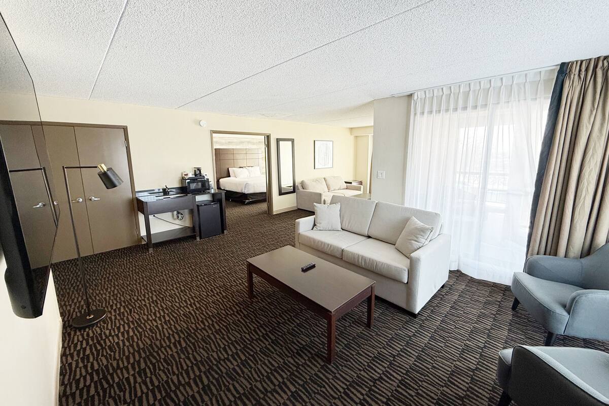 Ein Hotelzimmer mit Bett, Sofa, Schreibtisch mit Computer, Fernseher und Minibar.