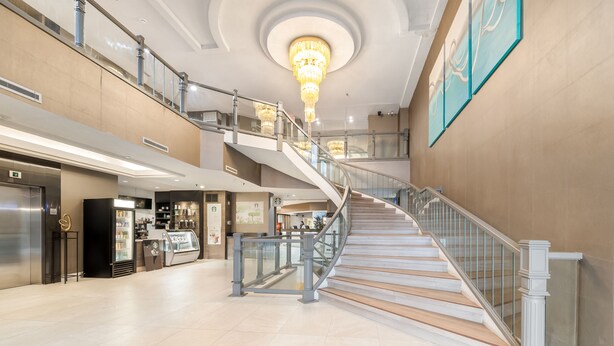 Un lobby espacioso con una imponente escalera, una cafetería y un candelabro.