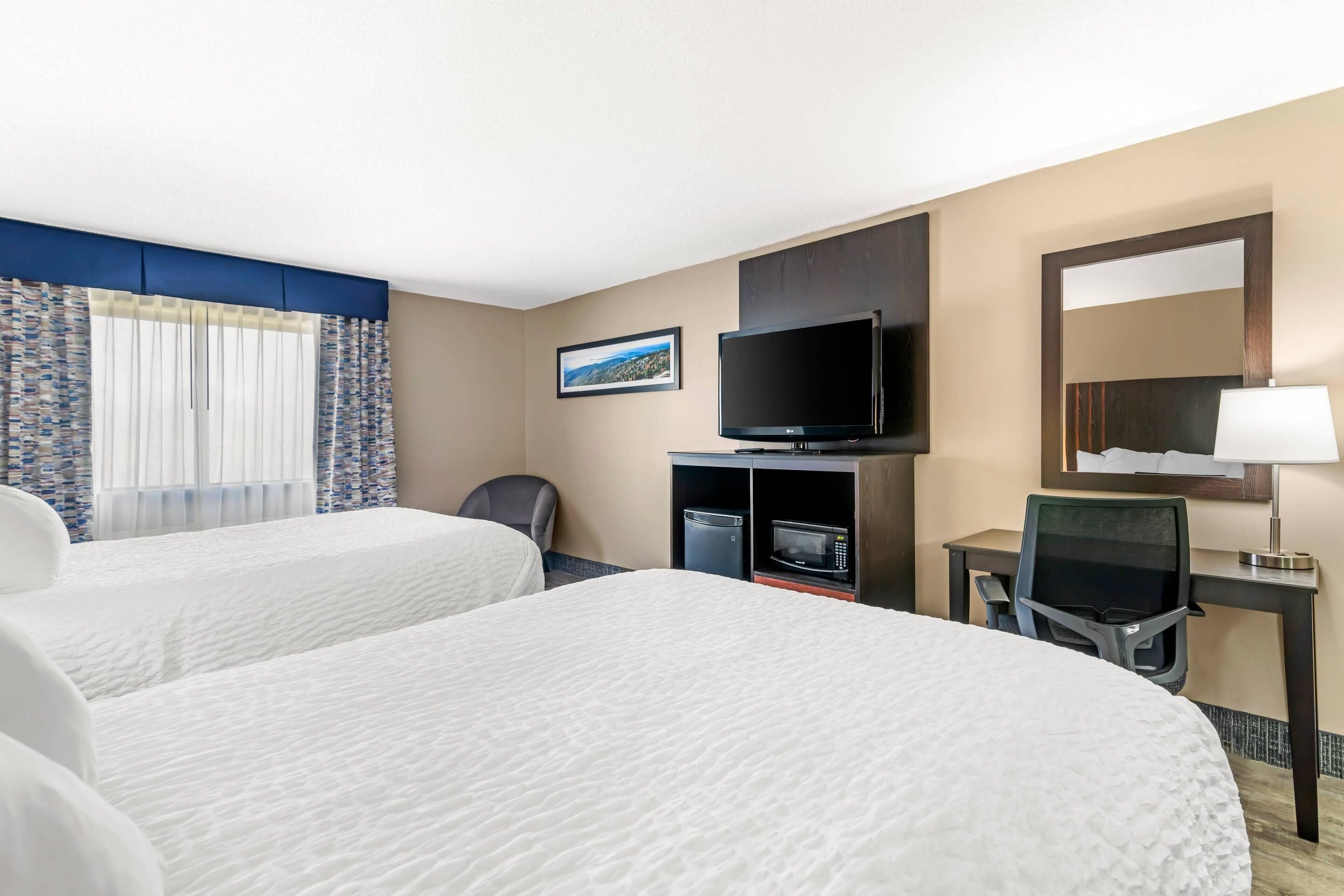 Habitación de hotel con dos camas, televisión, escritorio con silla y ventana con cortinas.