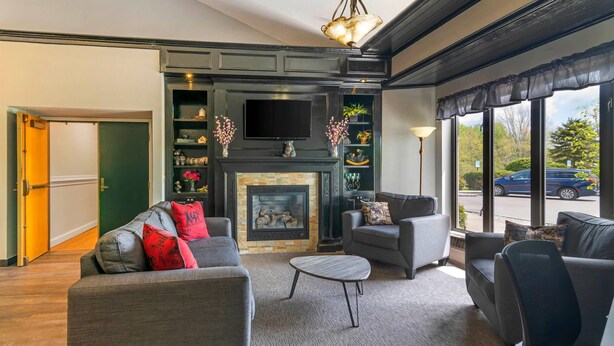 A modern living room with a fireplace, grey sofas, and a flat-screen TV mounted above it. - Black Bear Inn, an Ascend Collection Hotel (Orono)