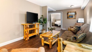 A living room with a wooden coffee table, a television on a wooden stand, a sofa with patterned cushions, and a door leading to a bedroom. - Black Bear Inn, an Ascend Collection Hotel (Orono)
