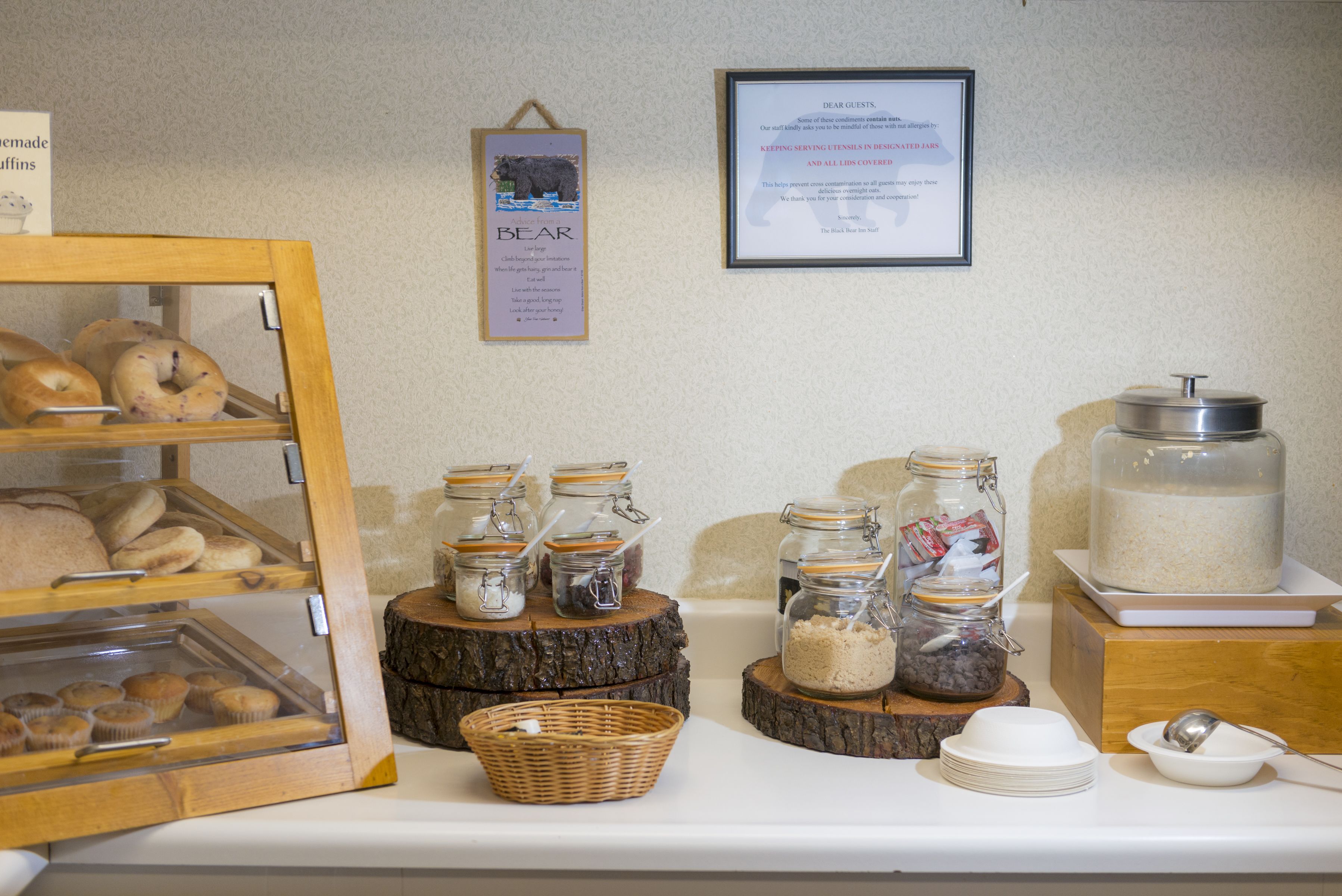 Un buffet della colazione con diversi prodotti da forno, vasetti di condimenti e un cartello che indica dove vanno tenuti gli utensili.