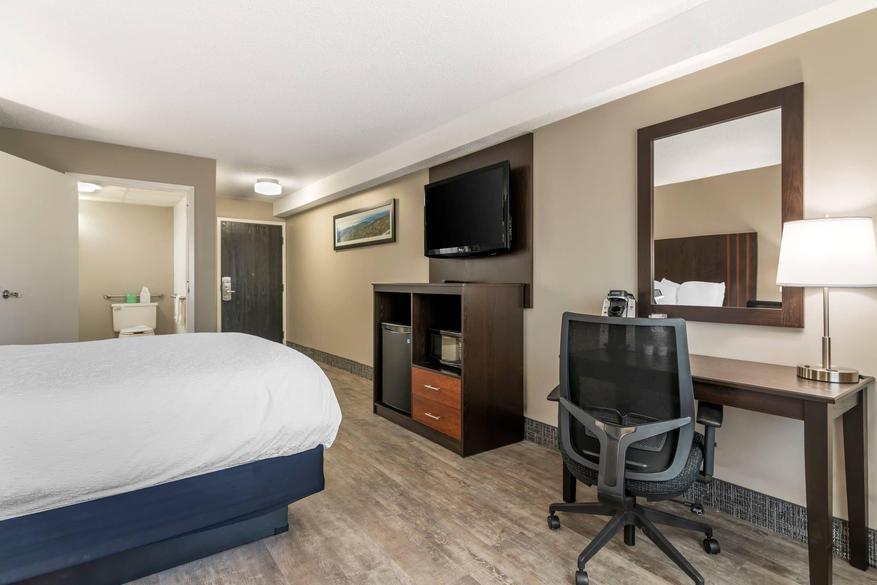 Een hotelkamer met een bed, een bureau met een computer, een stoel, een televisie en een spiegel.