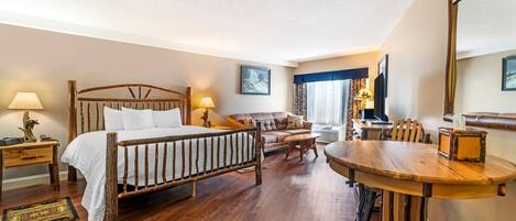 A hotel room with a wooden bed, a sofa, a dining table, and a TV.