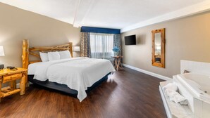 A hotel room with a wooden bed, a white bathtub, a flat-screen TV, and a large mirror. - Black Bear Inn, an Ascend Collection Hotel (Orono)