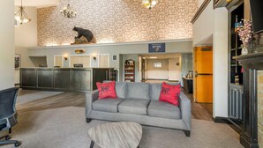 A modern lobby with a grey sofa, red pillows, a wooden coffee table, and a stone wall. - Black Bear Inn, an Ascend Collection Hotel (Orono)