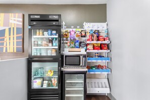 A compact kitchenette with a refrigerator, freezer, microwave, and a small pantry area.