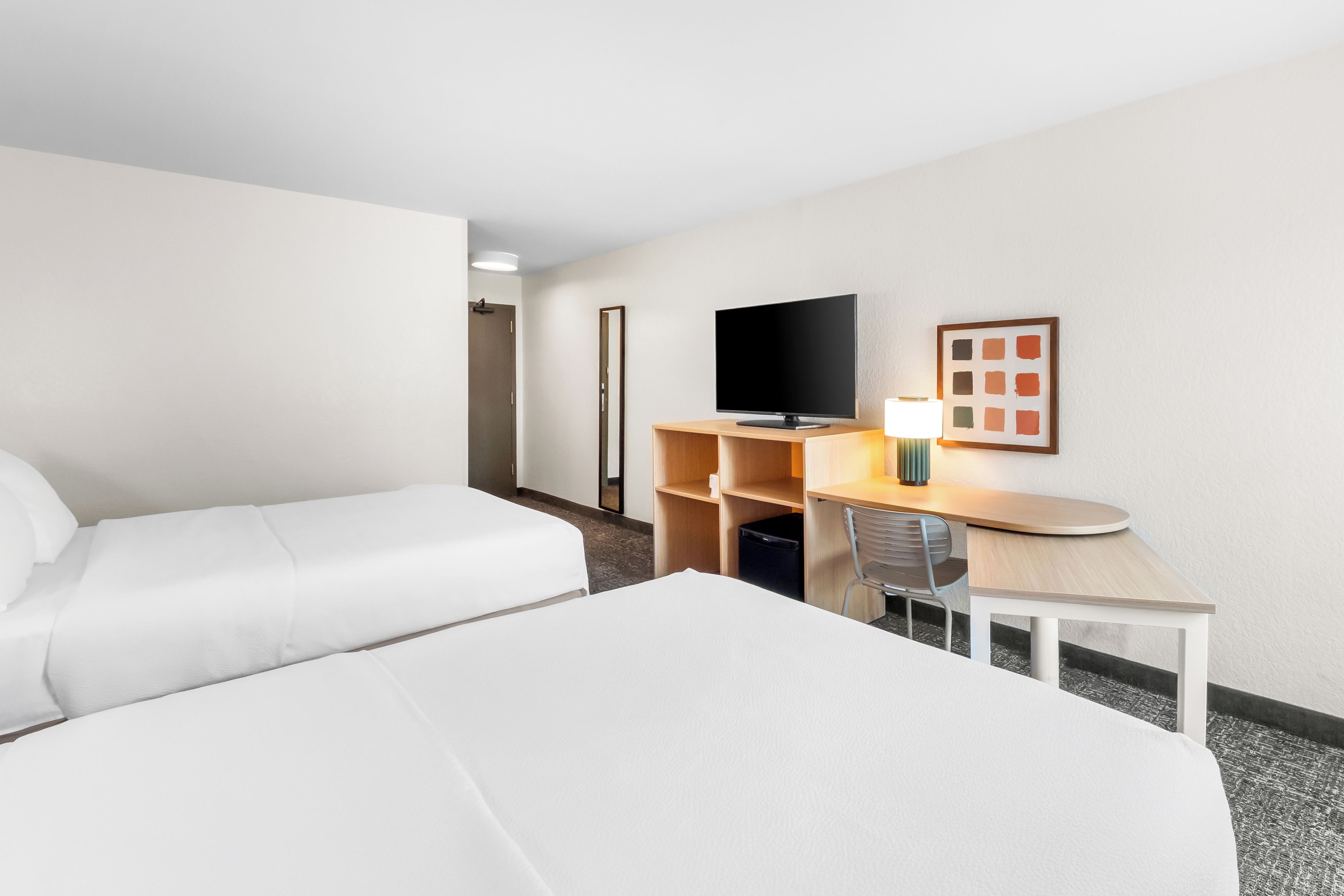 A hotel room with two beds, a desk with a computer, a TV, and a framed picture on the wall.