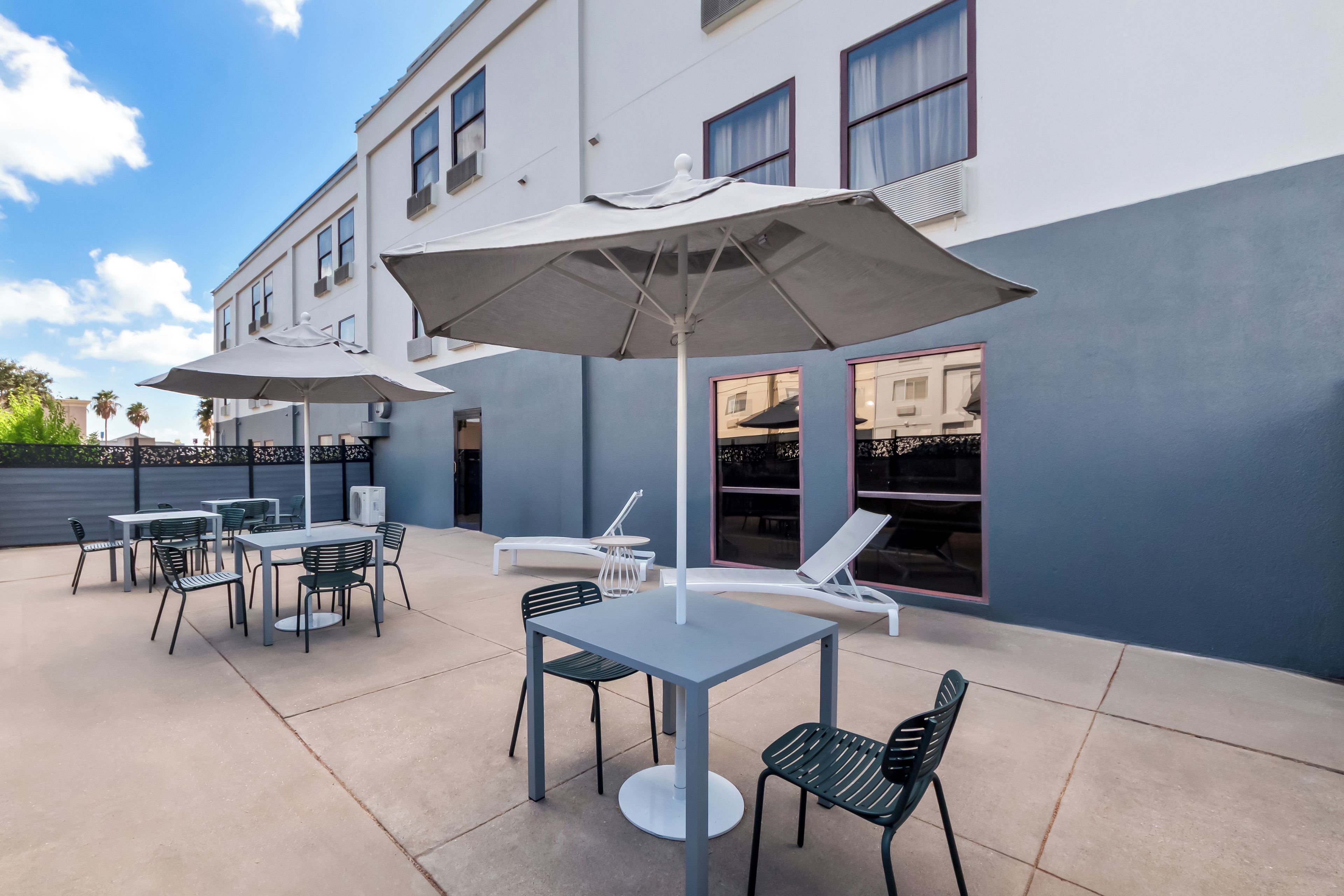 An outdoor patio with tables and chairs, umbrellas, and a pool area.