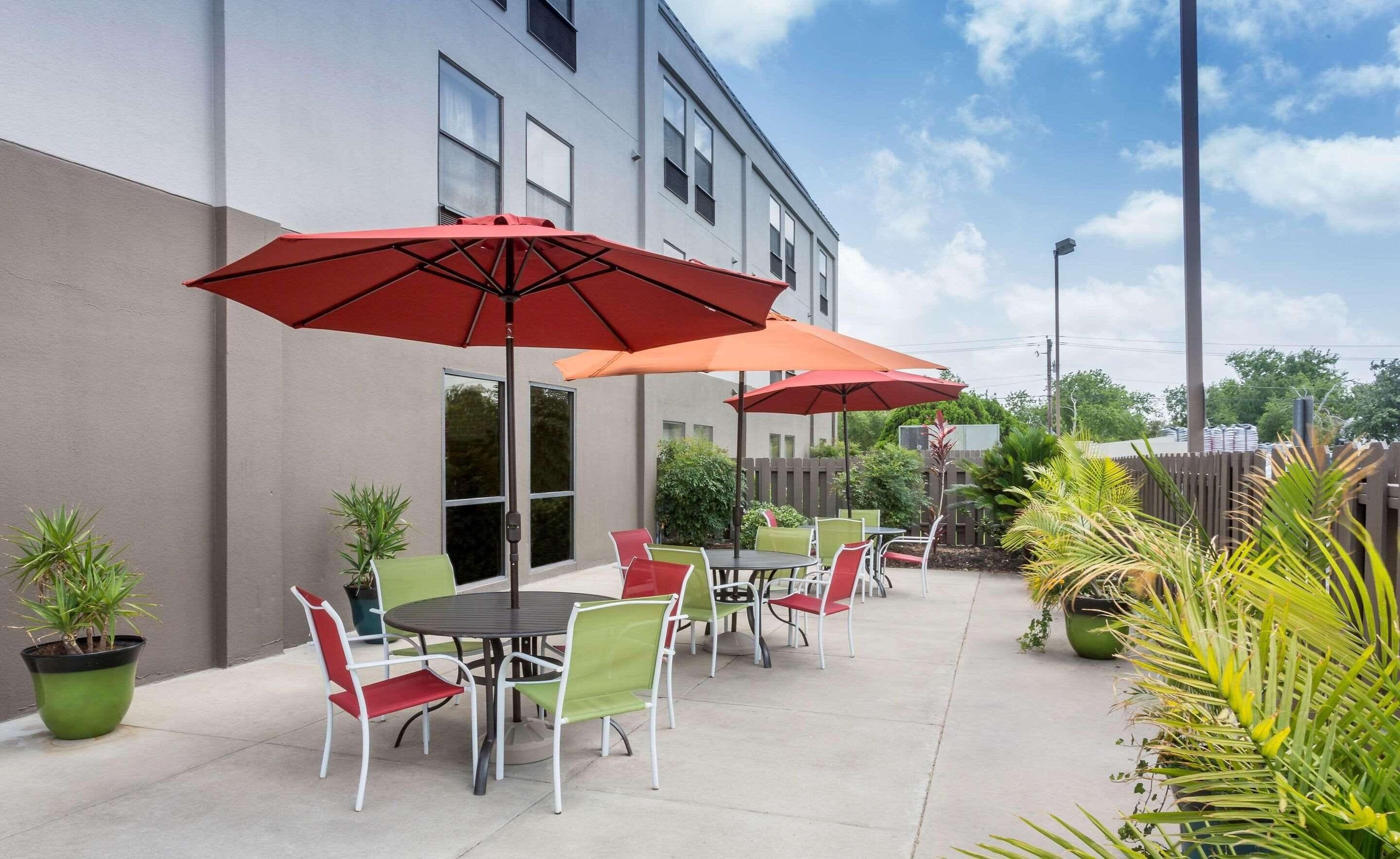 An outdoor patio with tables and chairs, red umbrellas, and potted plants.