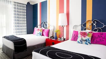 A hotel room with two beds, striped walls, a window with patterned curtains, and a bedside table with a lamp and phone.