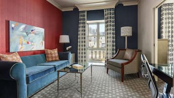 Una sala de estar con un sofá azul, un sillón estampado, una mesa de centro de vidrio y un cuadro en la pared.