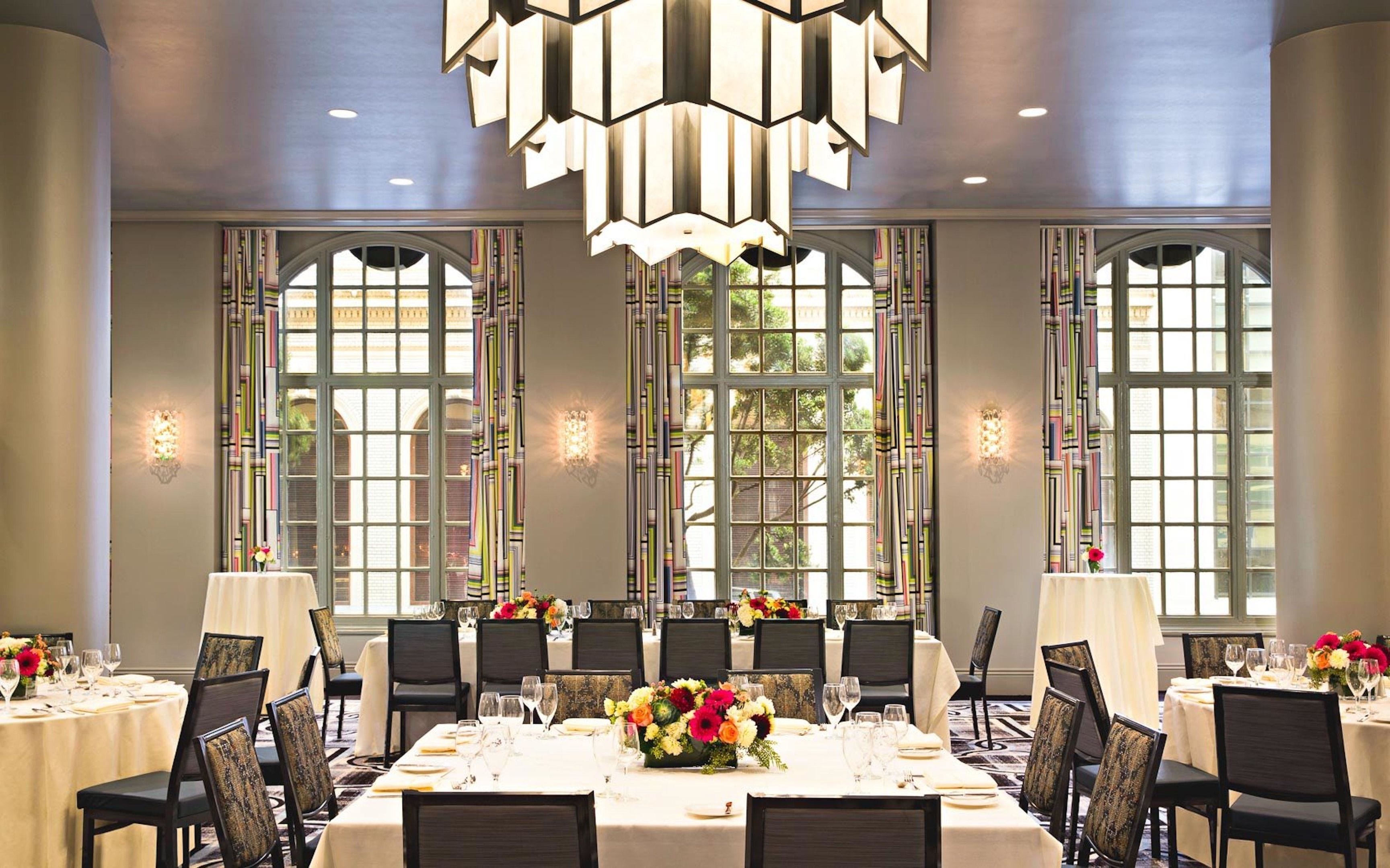 A dining area with tables set for service, large windows, and a modern chandelier.