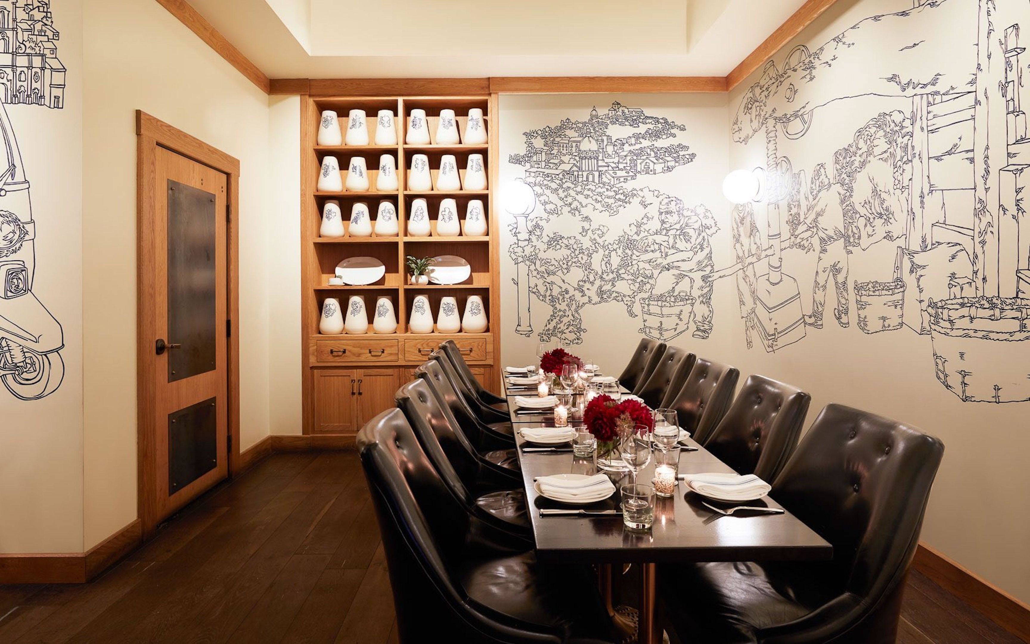 A dining area with a long table set for four, surrounded by black leather chairs. A wooden cabinet with white and blue patterned vases is against the wall.