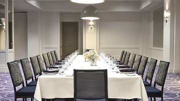 A conference room with a long table set for a meeting, surrounded by chairs, with a chandelier above.