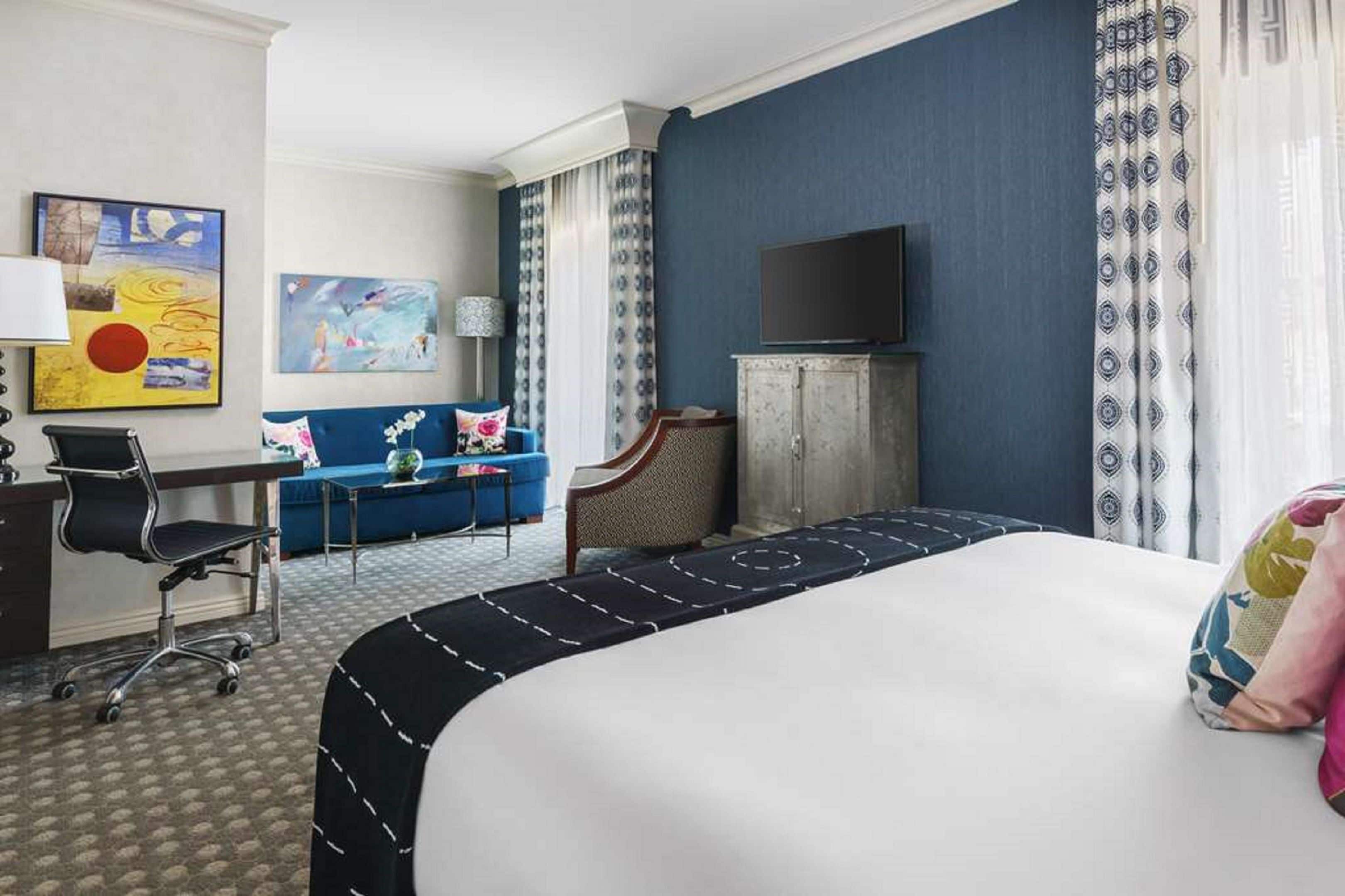 A hotel room with a bed, a desk, a chair, a television, and artwork on the walls.