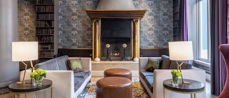 A modern living room with a fireplace, sofas, ottomans, and a bookshelf.